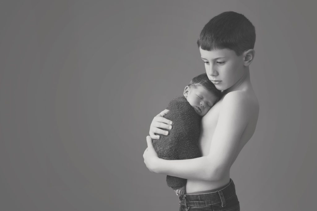 black and white image of boy holding newborn baby brother by Alyssa Joy Photography