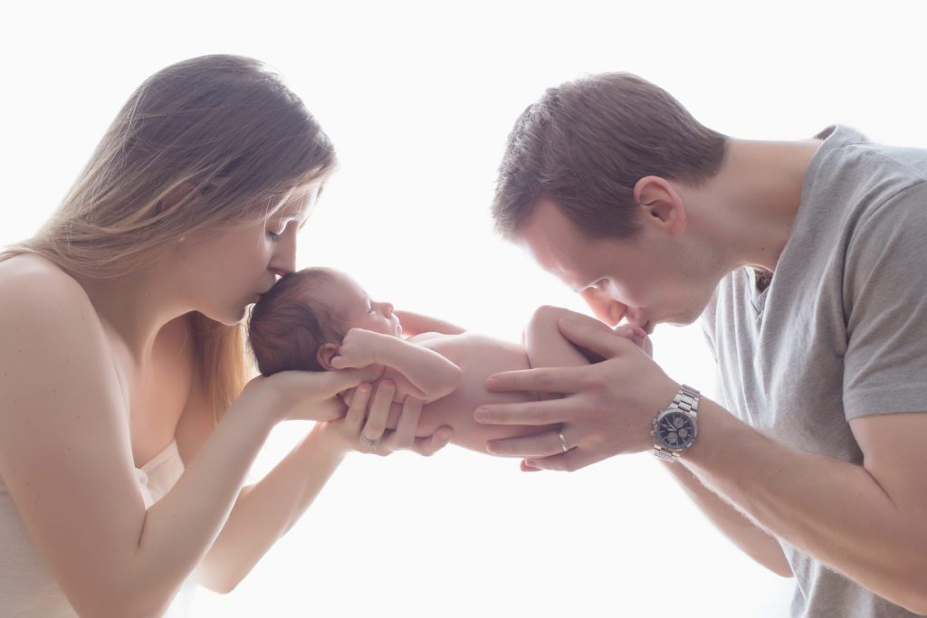 backlit image of mom and dad holding their newborn baby boy and kissing him by Alyssa Joy Photography