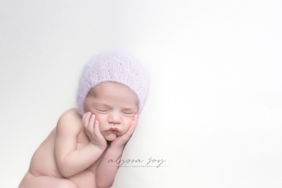 newborn baby girl on white background with lilac bonnet