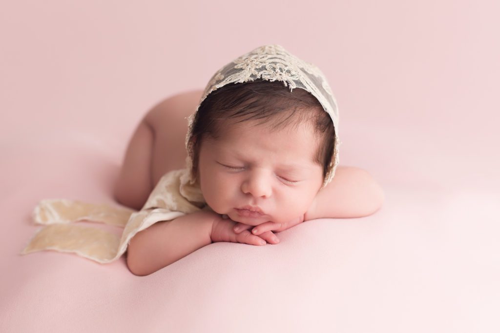 newborn baby girl portrait facing forward with lace bonnet on pink