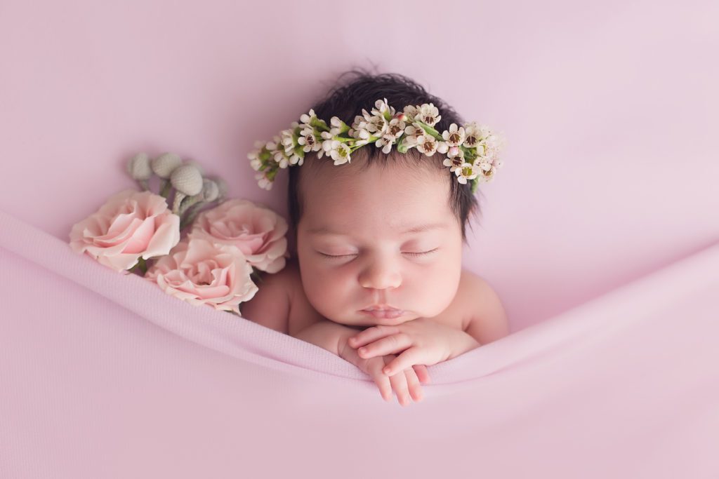 newborn girl with fresh flowers and floral halo on pink