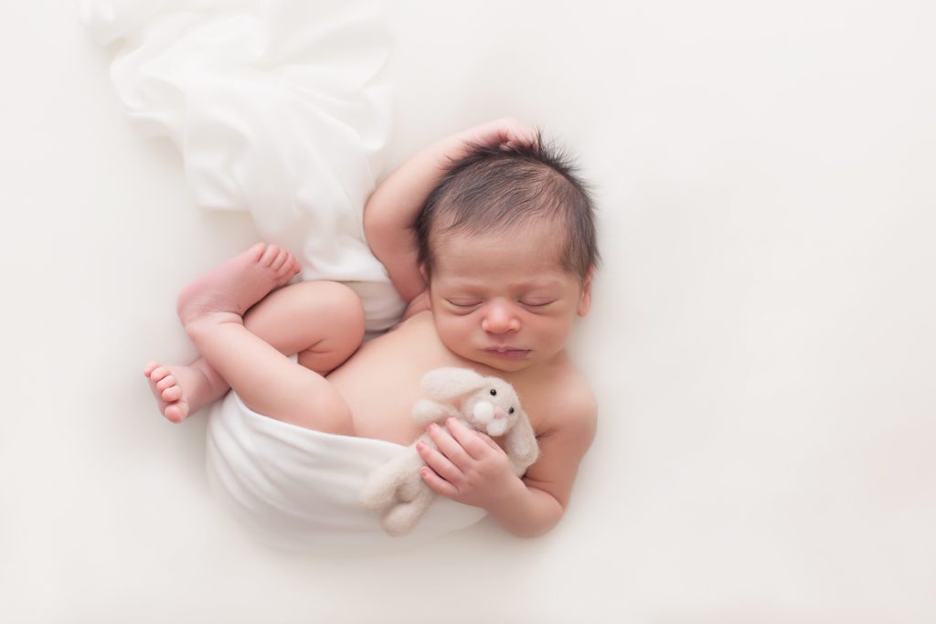 newborn girl simply posed on white holding little felted bunny