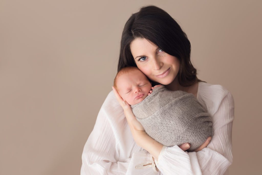 portrait of mom with newborn baby boy wrapped in grey