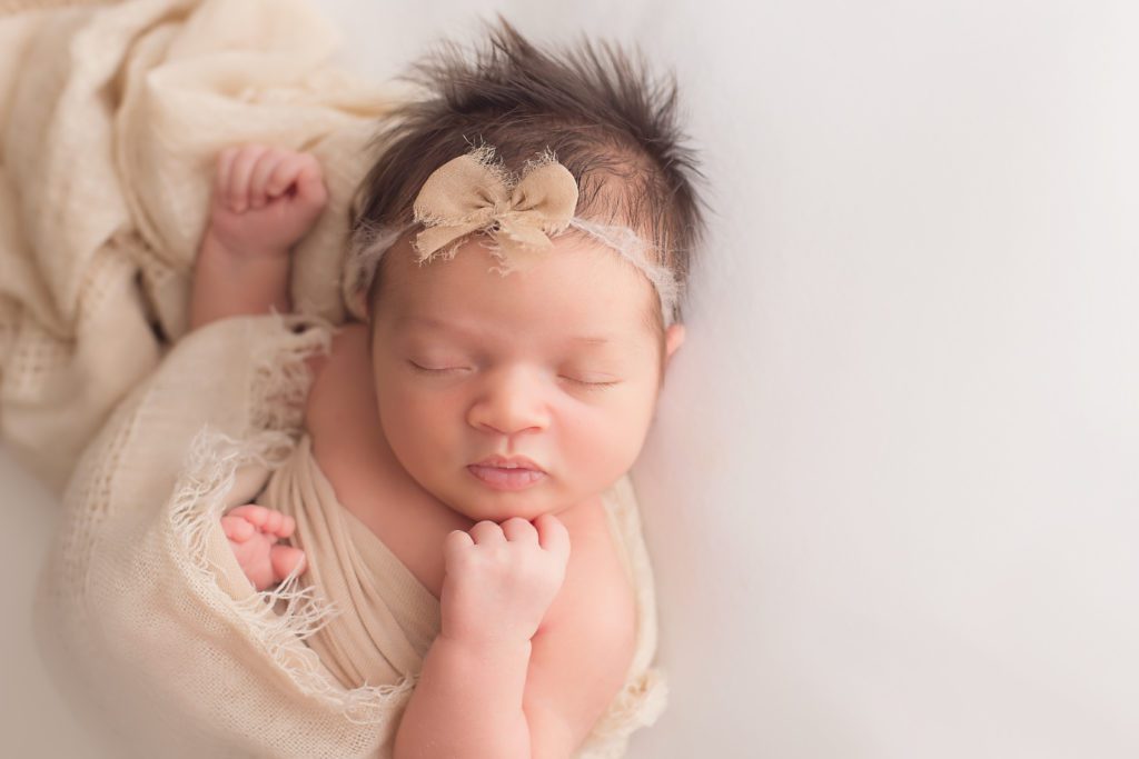 newborn baby girl wrapped in cream organic wrap and posed with cream bow