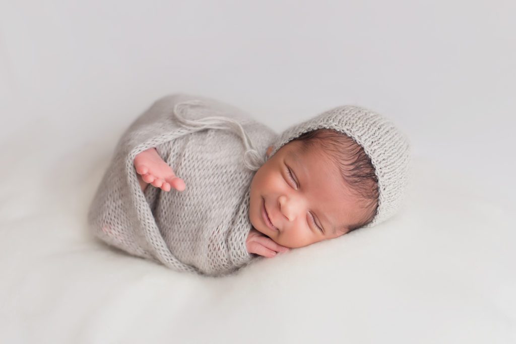 newborn baby boy wrapped in grey and smiling