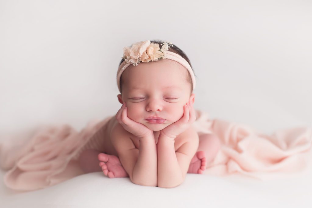 picture of newborn baby girl in froggy pose with pink headband and wrap