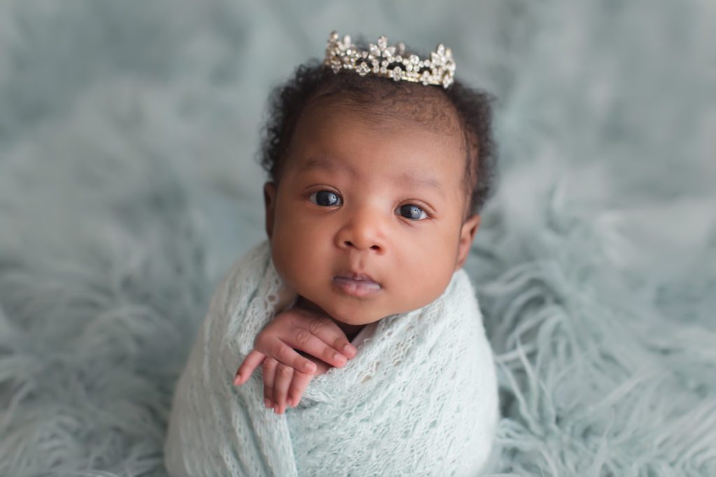 newborn baby girl wrapped in potato sack pose and little princess crown with eyes open