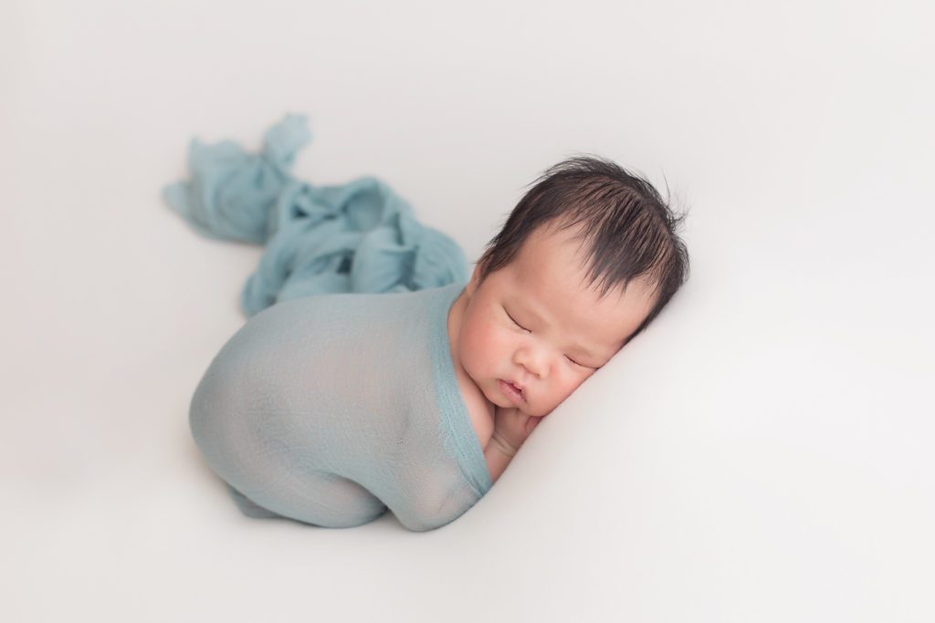 newborn baby boy wrapped in blue sheer wrap posed on neutral backdrop Alyssa Joy Photography