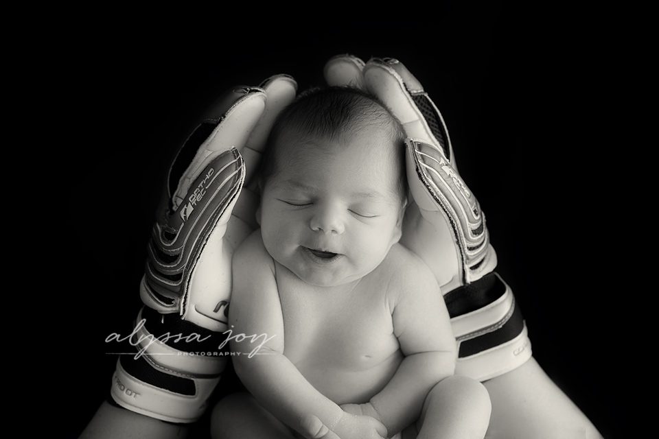 black and white picture of baby girl being held in dad's soccer gloves