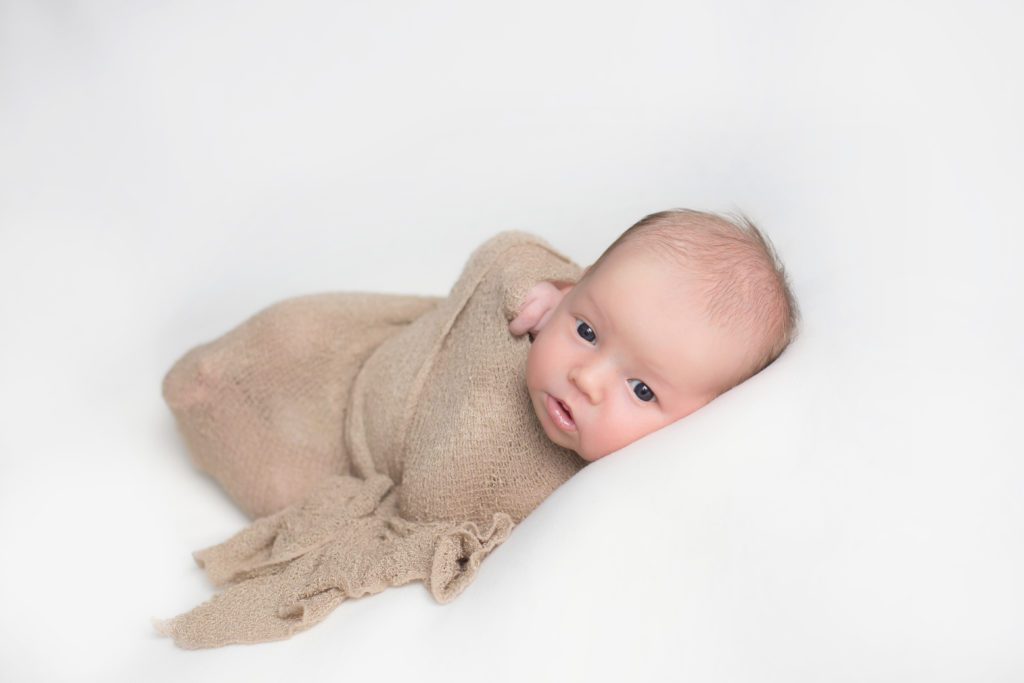photo of 18 day old baby boy wrapped in beige wrap with eyes open