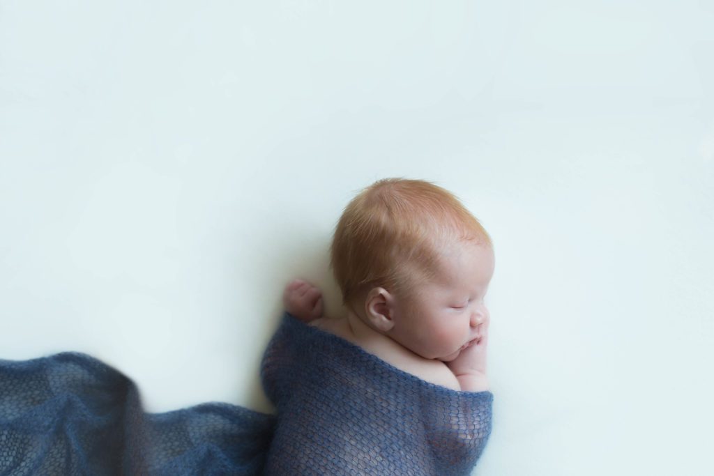 photo of top half and side view of red headed baby boy wrapped in dark blue