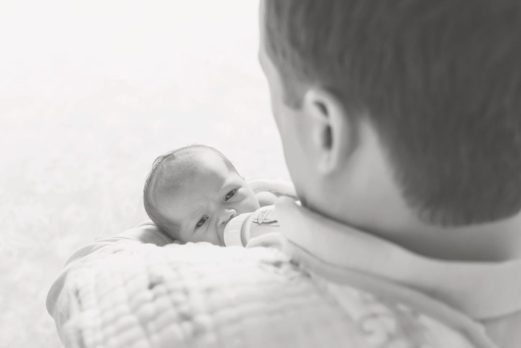 black and white photo of new dad feeding a bottle to newborn baby girl