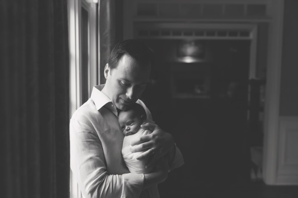 black and white image of new father holding newborn baby girl lifestyle session