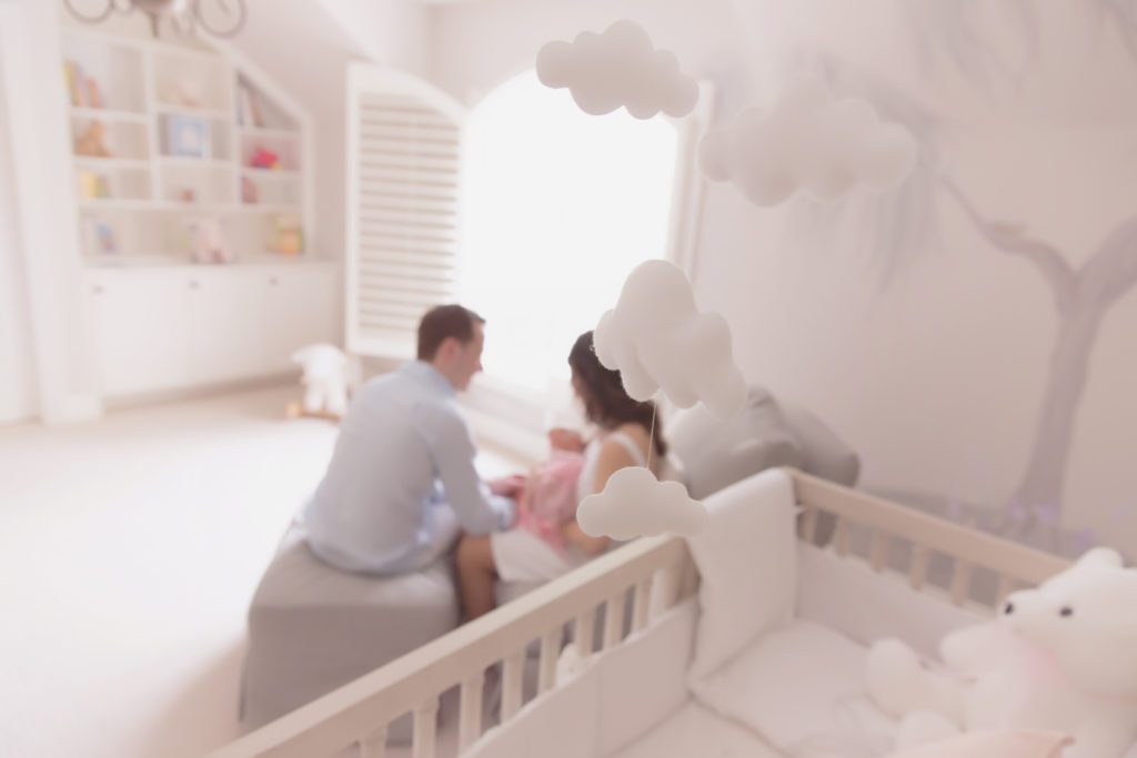photo of nursery with mom and dad sitting on rocker holding baby in the background