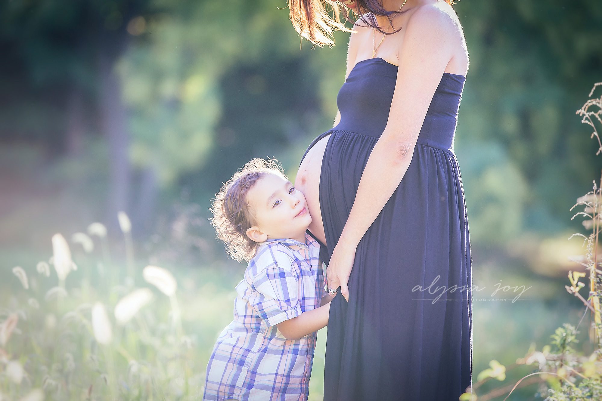 image of big brother listening to his baby sister in mommy's belly in beautiful field