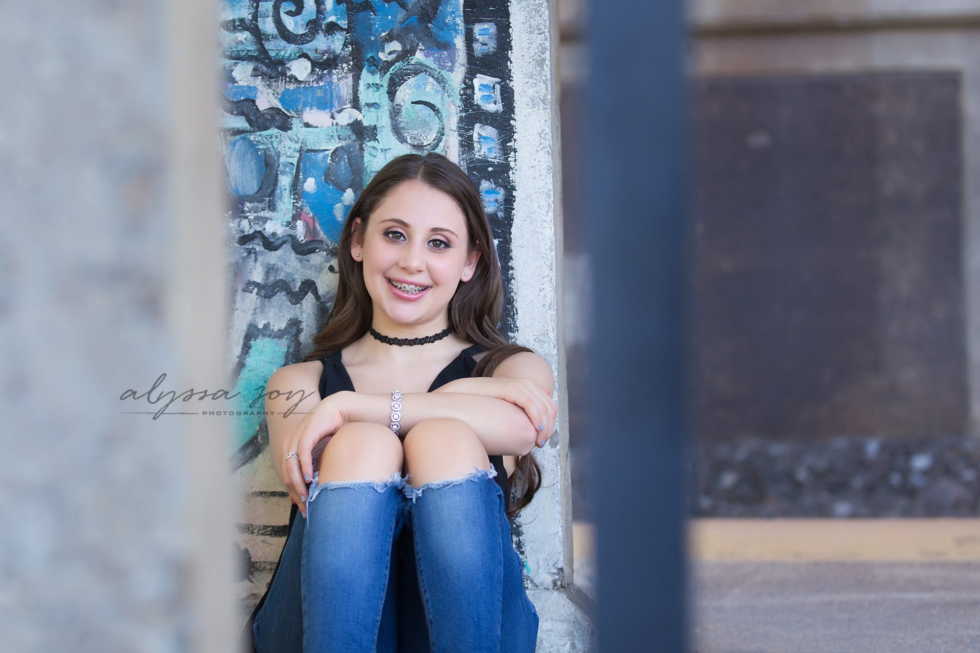 blue and green graffiti wall with teenage girl sitting and smiling