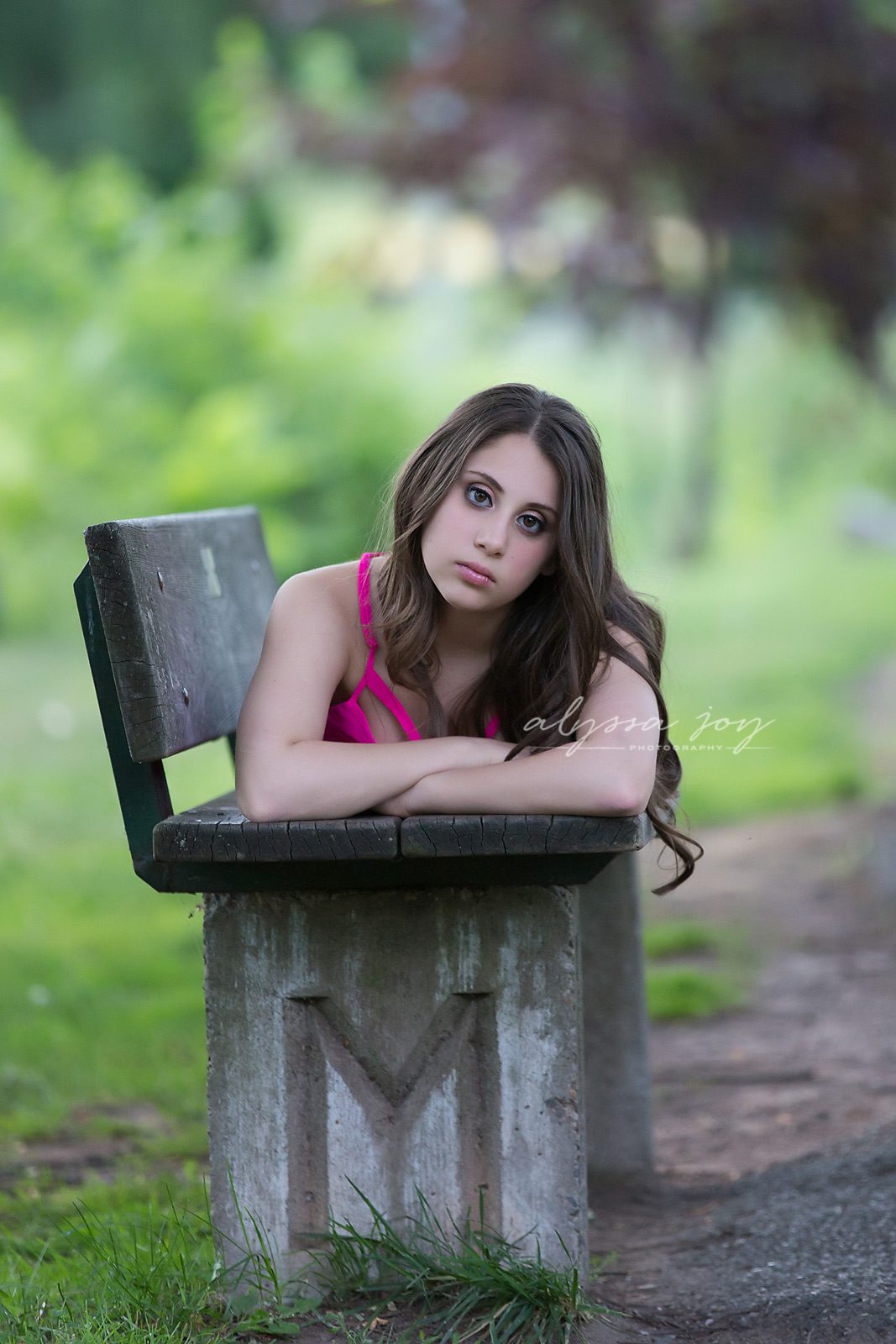 teen girl laying on a bench in the park with her first initial engraved into the bench
