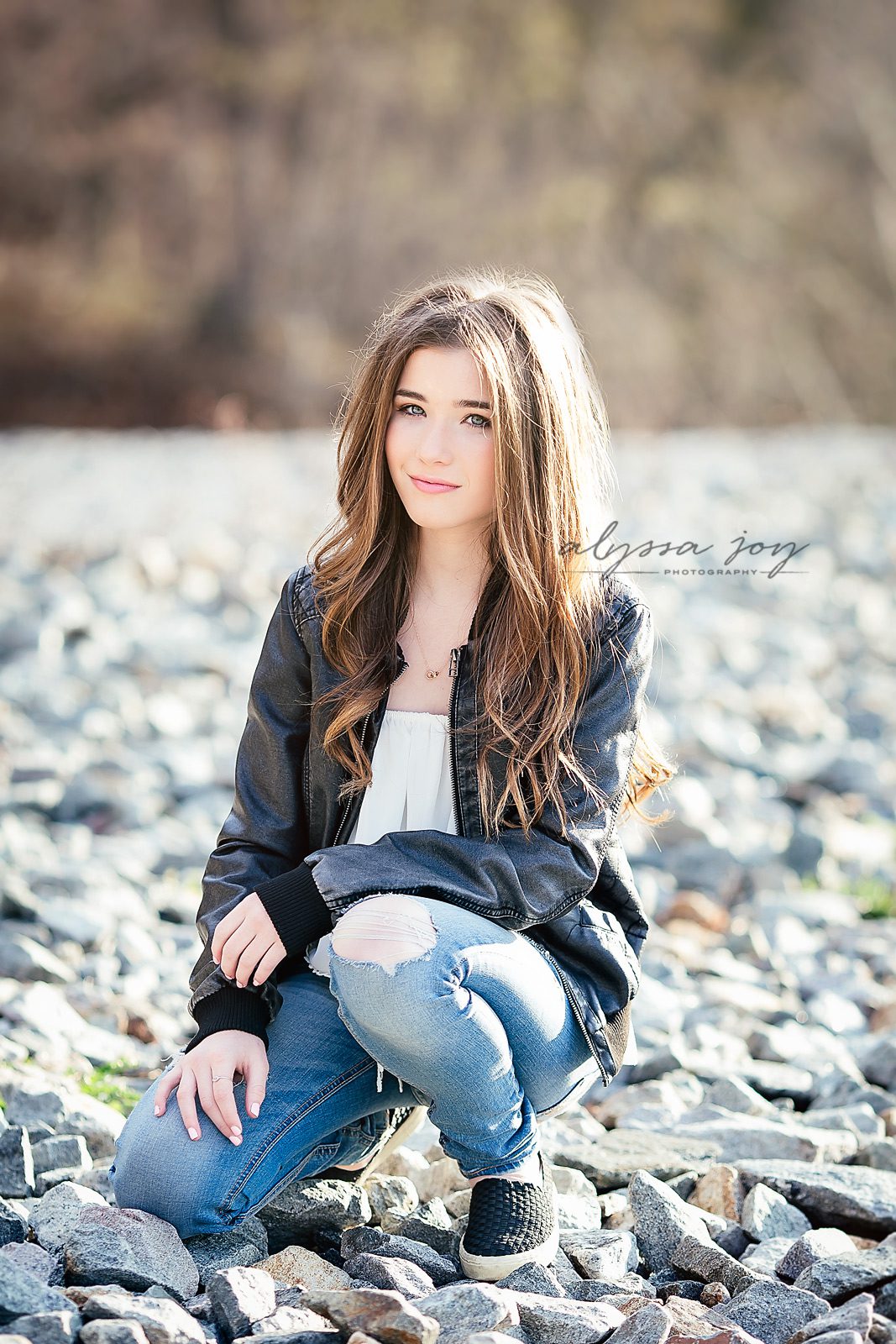 teenage girl kneeling on rocks on a sunny day on location Alyssa Joy Photography