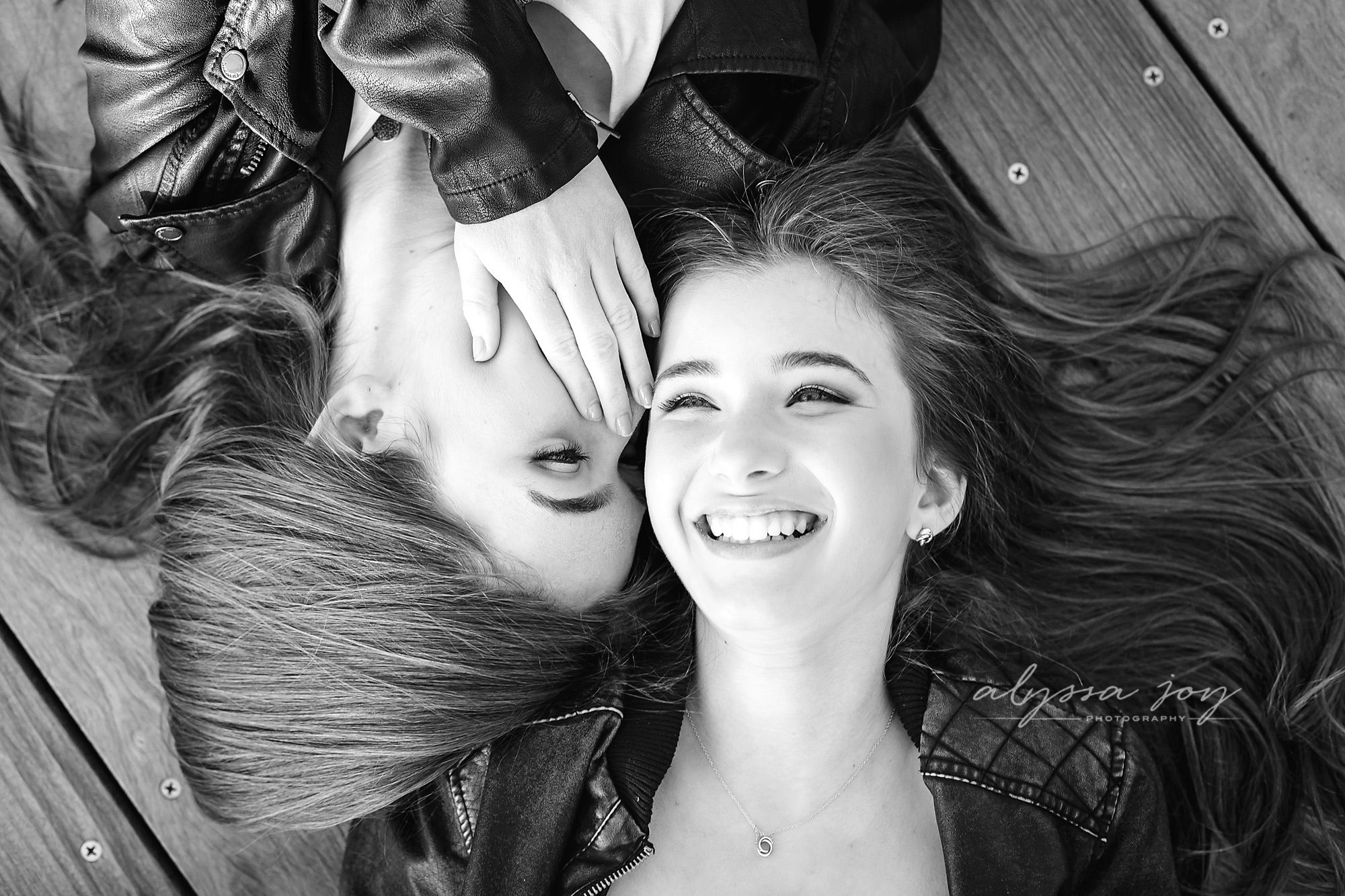 two teenage sisters telling a secret on boardwalk black and white shot by Alyssa Joy Photography