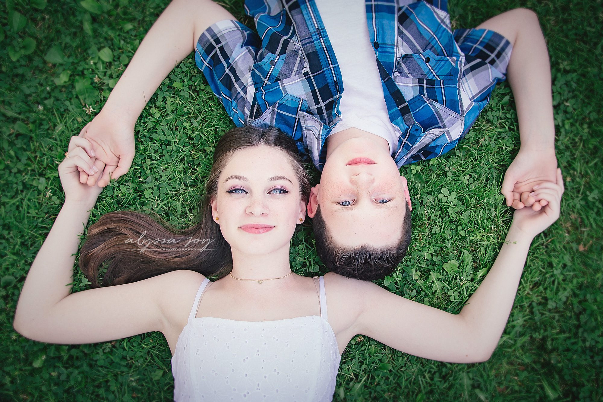photo of teenage brother and sister laying on grass, holding hands and looking up for Alyssa Joy Photography