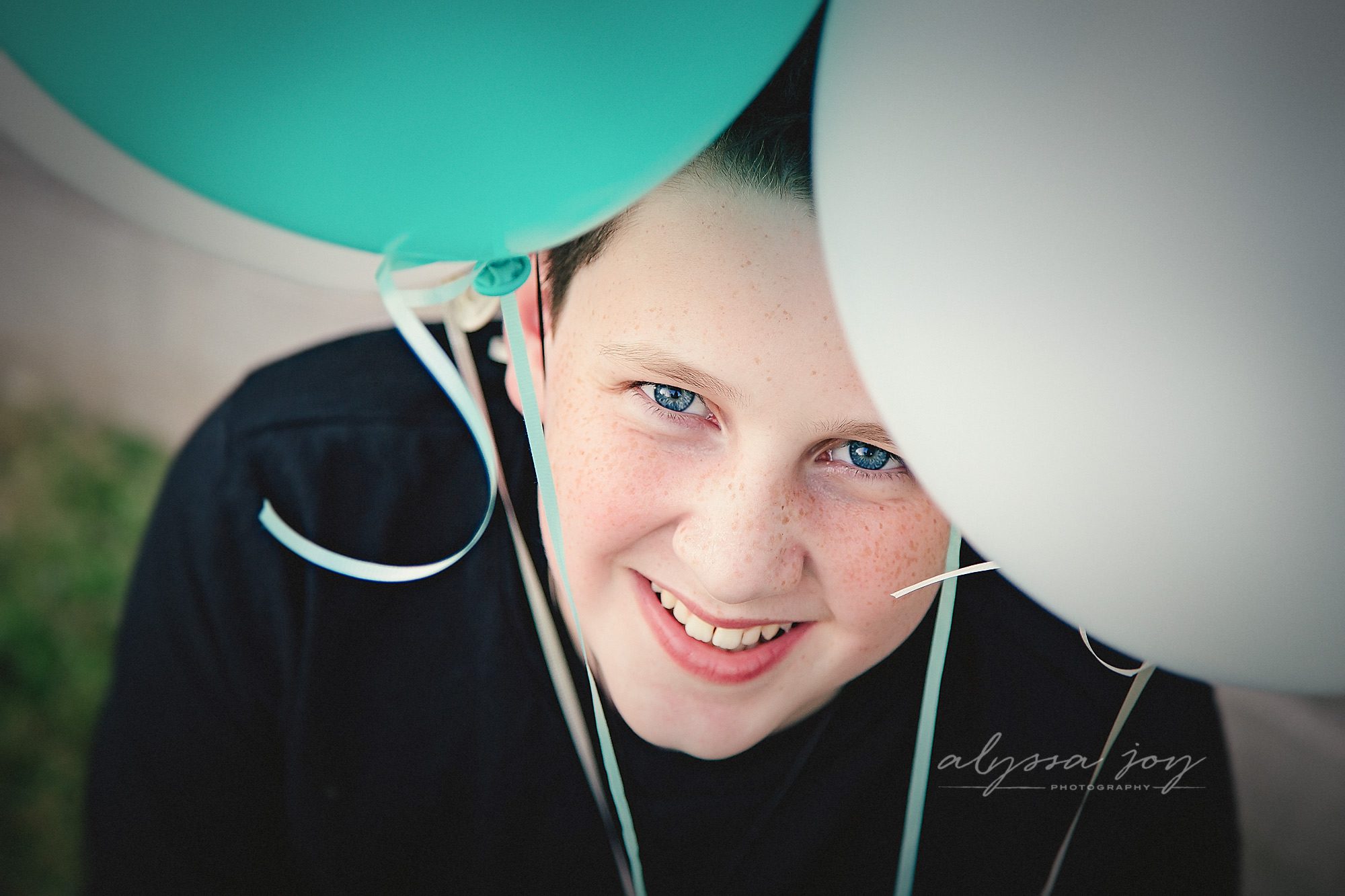 teenage boy smiling and peeking through balloons posing for Alyssa Joy Photography