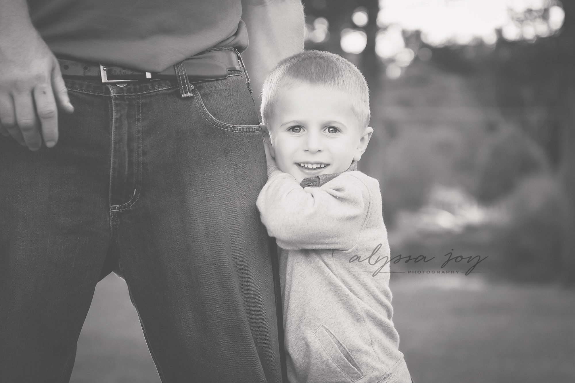 black and white image of young boy holding onto dad's leg 