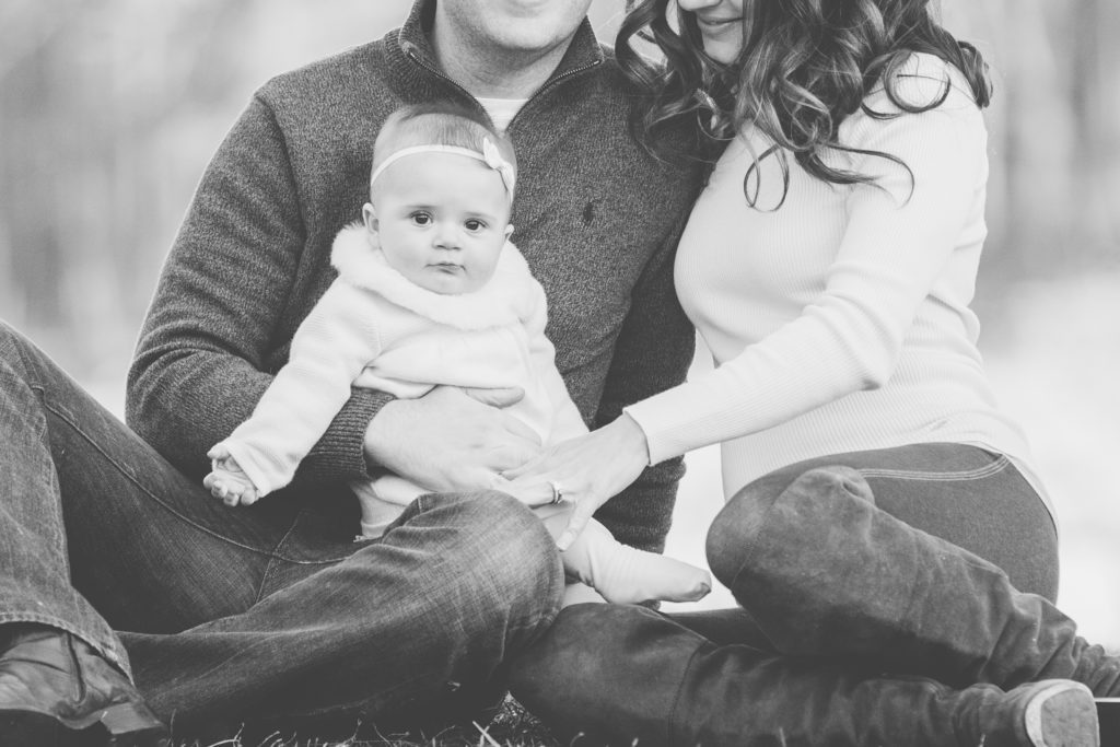 black and white photo of 6 month old baby girl sitting on mom and dad's lap at family photo session in park in New Jersey