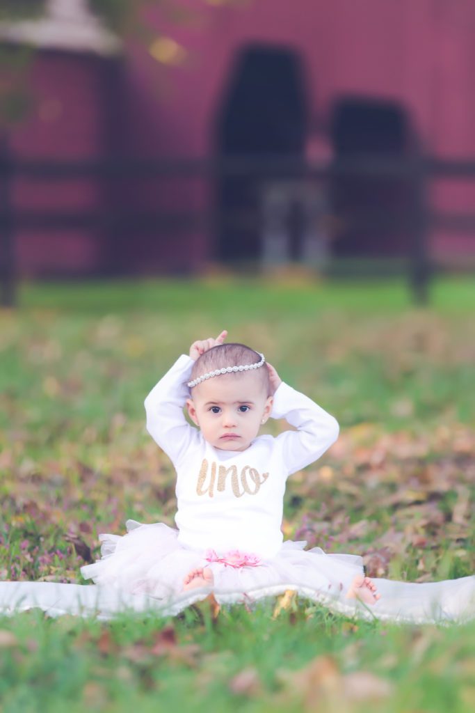 picture of one year old milestone session little girl sitting on grass with pink tutu and "uno" shirt