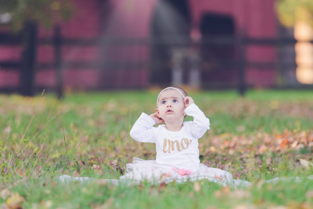little girl sitting in grass with an "uno" shirt on looking up at the sky one year milestone photo session