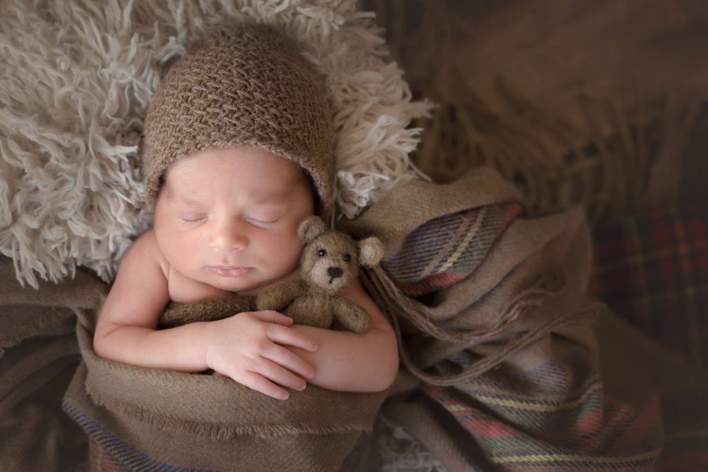 Newborn baby boy holding brown teddy bear 