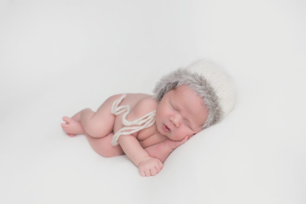 newborn baby boy with eskimo hat on white fabric by Alyssa Joy Photography
