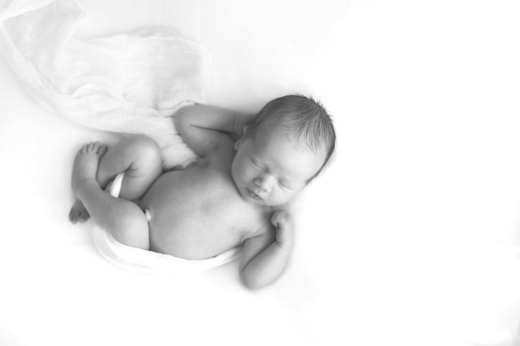 black and white photo of newborn baby boy on back wrapped in fabric