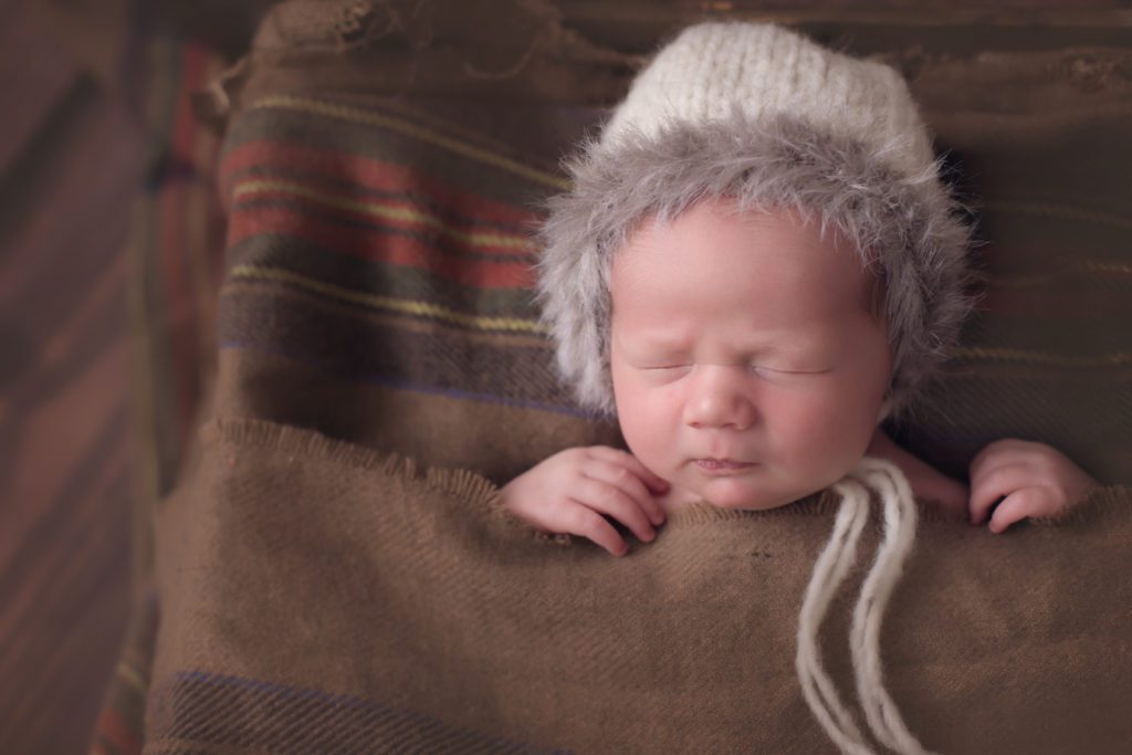 newborn baby boy posed in crate with winter blanket and eskimo bonnet