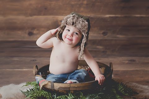 first birthday photo woodland theme photo session of one year old boy wearing blue jeans and faux fur hat