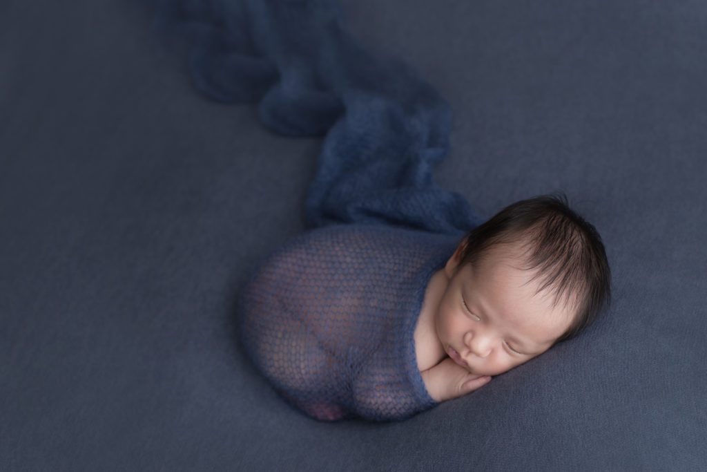 3 week old baby boy wrapped in navy on a navy backdrop simply posed by Alyssa Joy Photography