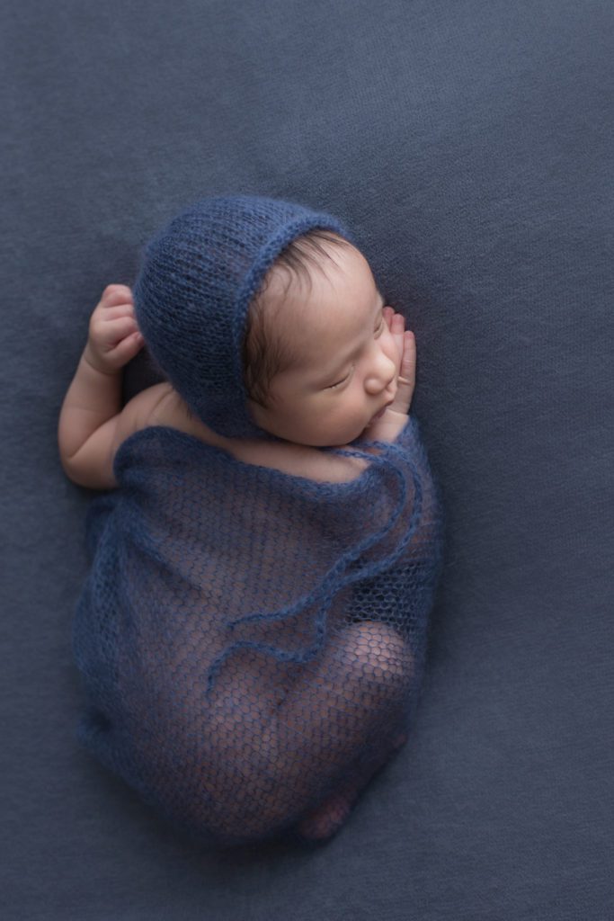 photo of baby boy 4 weeks old on navy blue in matching wrap and bonnet by Alyssa Joy Photography