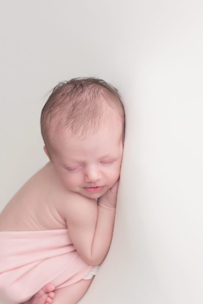 horizontal image of newborn baby girl in pink outfit on white backdrop