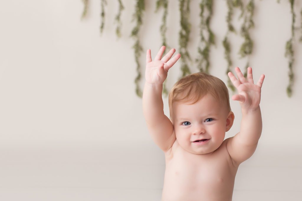 picture of one year old girl with hands up and smiling at one year photo session