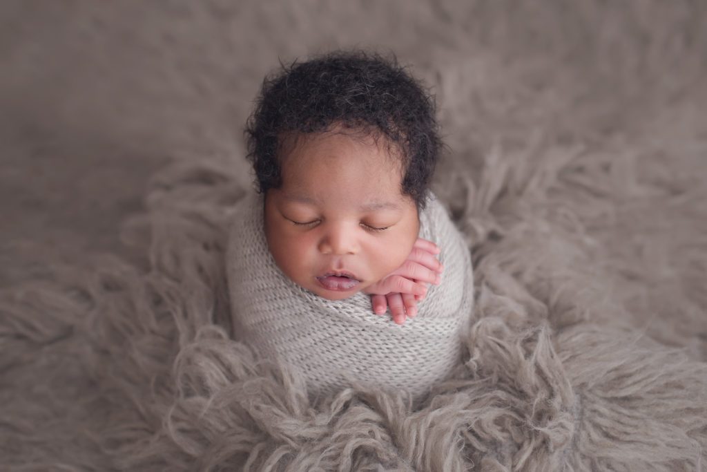 newborn boy wrapped in gray wrap on gray flokati rug
