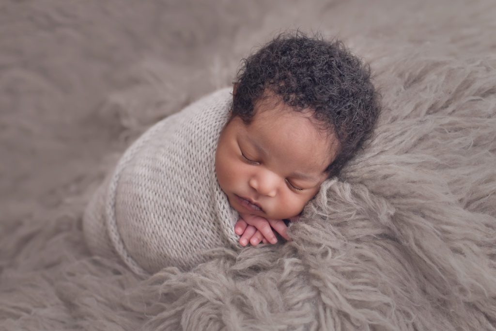 portrait of newborn baby boy in gray wrap laying on his side on a gray flokati rug