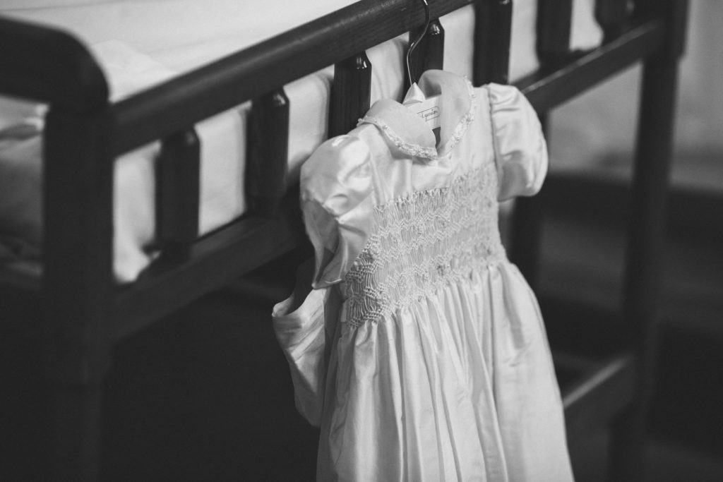 black and white picture of baptism dress hanging from wooden bassinet in church