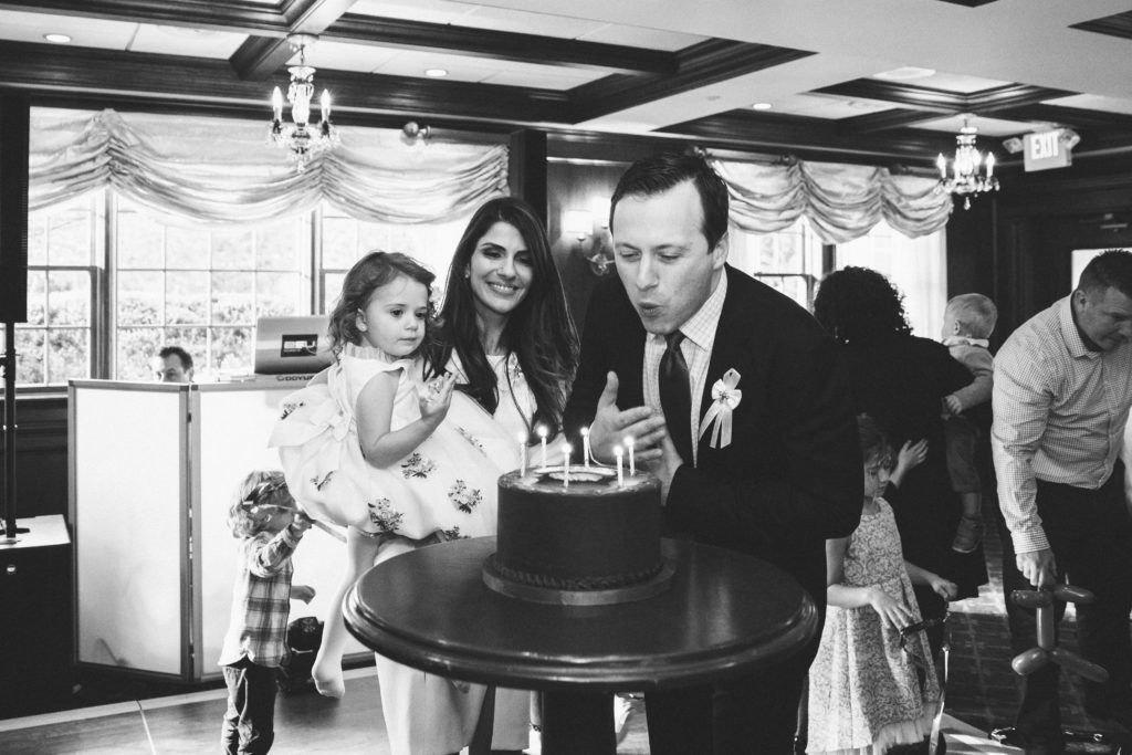 black and white photo of baby's father blowing out candles of his surprise birthday cake 
