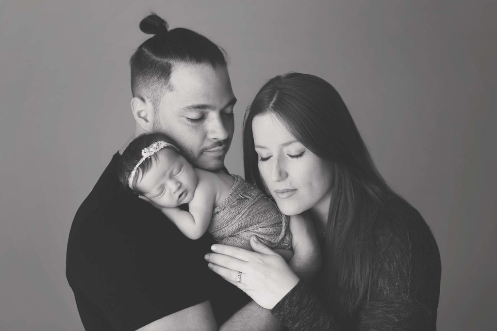 black and white photo of mom and dad holding newborn baby girl with eyes closed