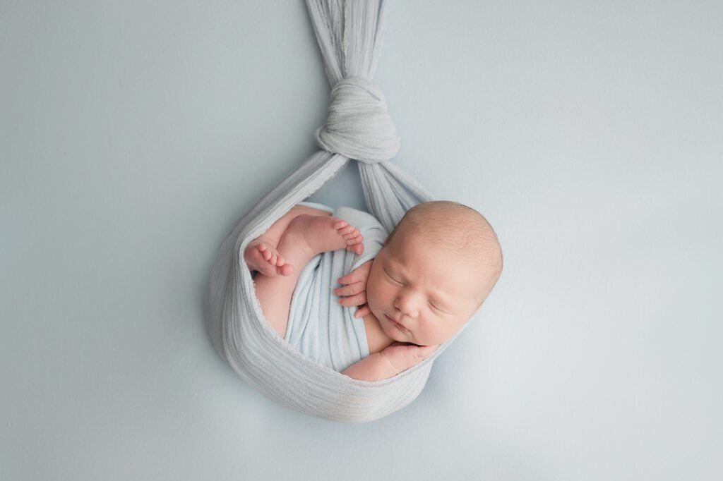 newborn boy posed and wrapped in baby blue stork wrap