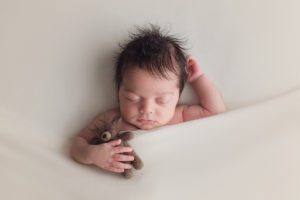 tucked in newborn baby boy holding brown bear