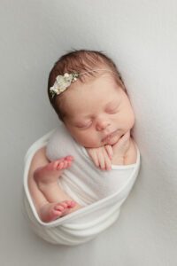 newborn baby girl wrapped in white with pretty white floral tieback