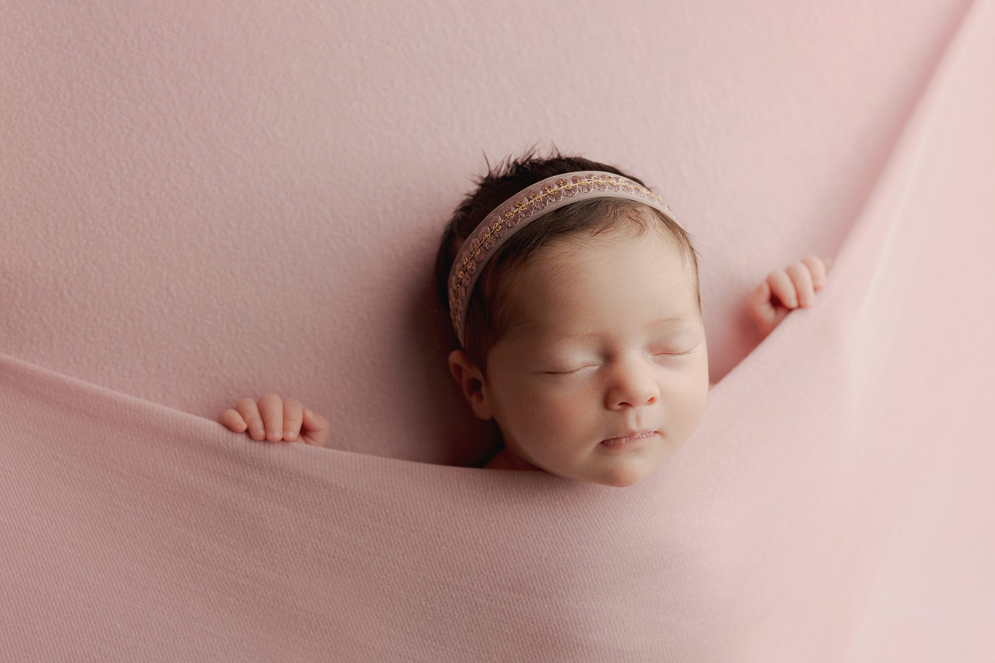 newborn baby girl cuddled up under pink blanket posed by Alyssa Joy Photography