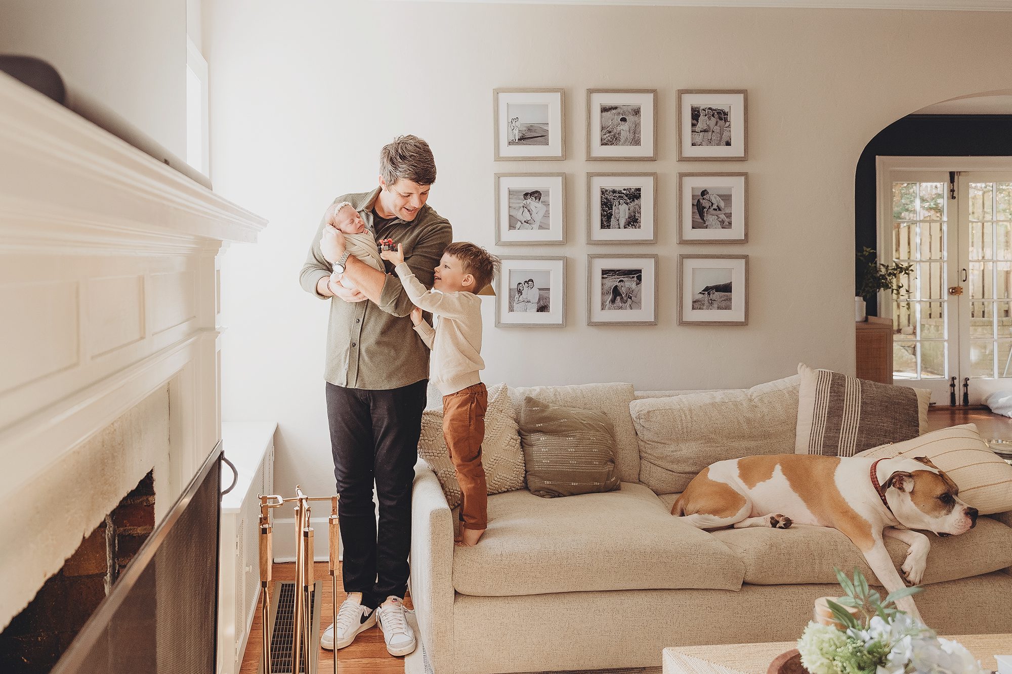 newborn lifestyle photo session dad holding newborn baby girl with older son looking on