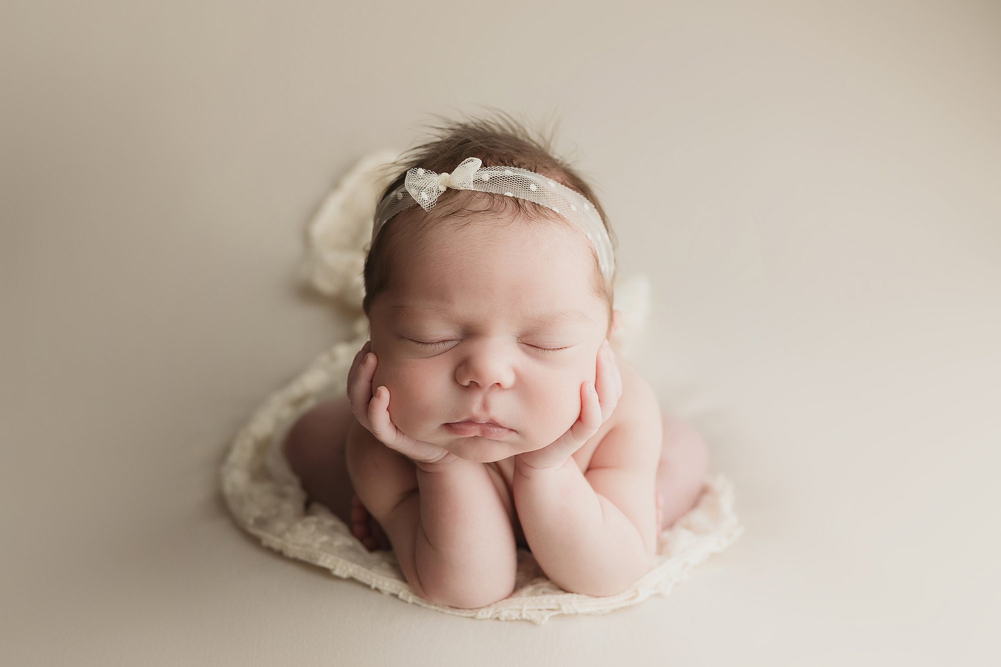 newborn baby girl posed on neutral fabric with bow headband froggy pose